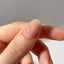 Close-up of a hand with a pink nail with gold flakes on a neutral background
