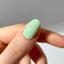 Close-up of a hand with a light green nail polish on a neutral background