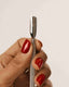 Hand holding a silver tool with red nail polish on a plain background